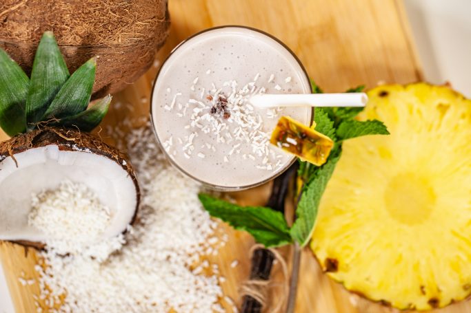 Kokosnuss- und Ananassaft mit Kokosraspeln auf Holzuntergrund.
